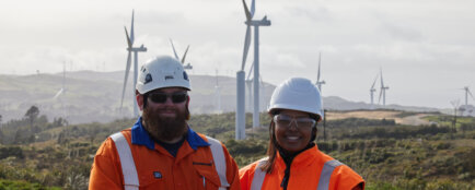 Two team members smiling in front of the wind farm
